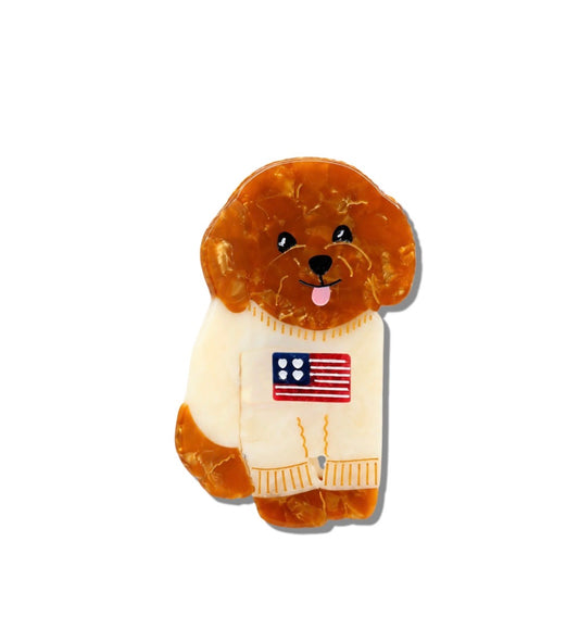 A small dog-shaped claw clip, featuring a brown and amber marbled texture. The dog is wearing a cream-colored sweater with a small American flag patch on the chest, set against a plain white background.