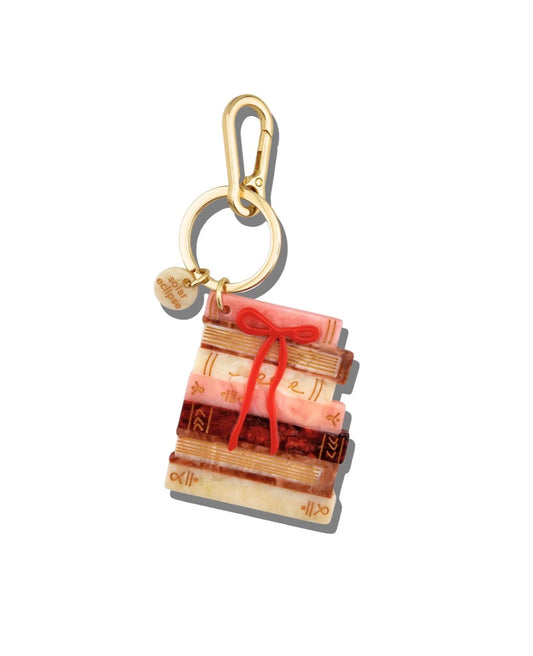 A gold-tone keychain charm shaped like a stack of books tied with a red string, featuring a small round gold tag, shown on a plain white background.