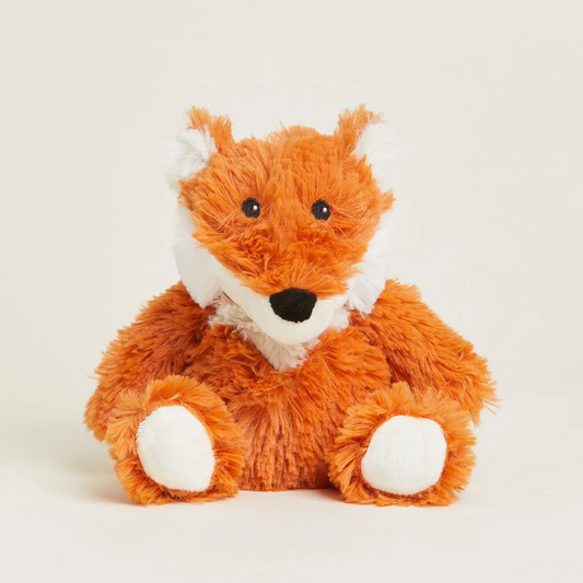 A plush toy fox made of soft orange-brown faux fur with white accents on its muzzle, inner ears, and paws, sitting against a plain light beige background.
