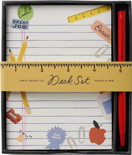 Rifle Paper Co. Desk Set in a black tray, featuring a lined notepad with colorful paper cutouts of school supplies and a red pen in the slot on the right.