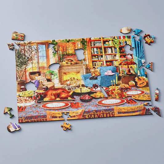 A completed and partially assembled jigsaw puzzle showing a cozy autumn living room and dining table scene, displayed on a light gray background with a few loose puzzle pieces around it.